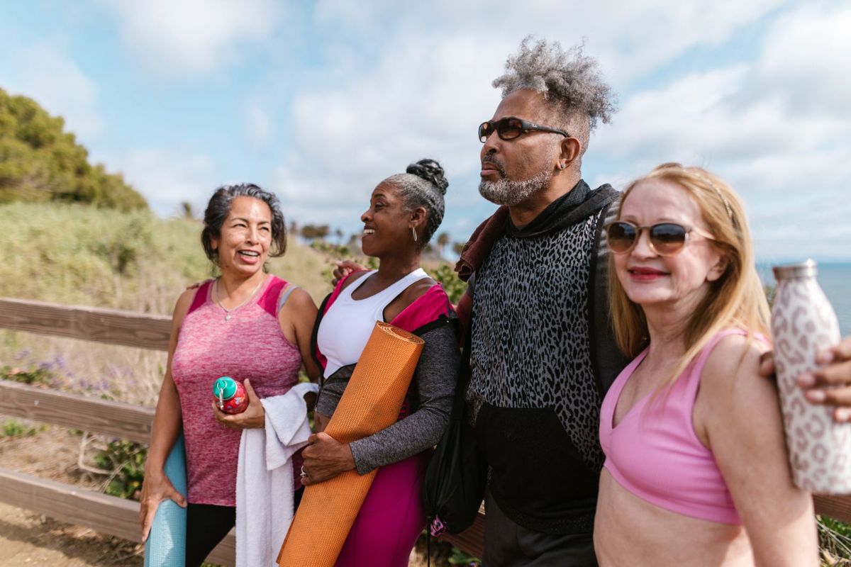 Four smiling older adult friends of different races walk together outdoors